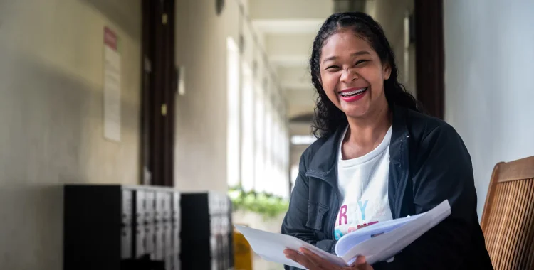 Mujer sonriendo con una hoja de vida en mano, participando en una feria de empleo