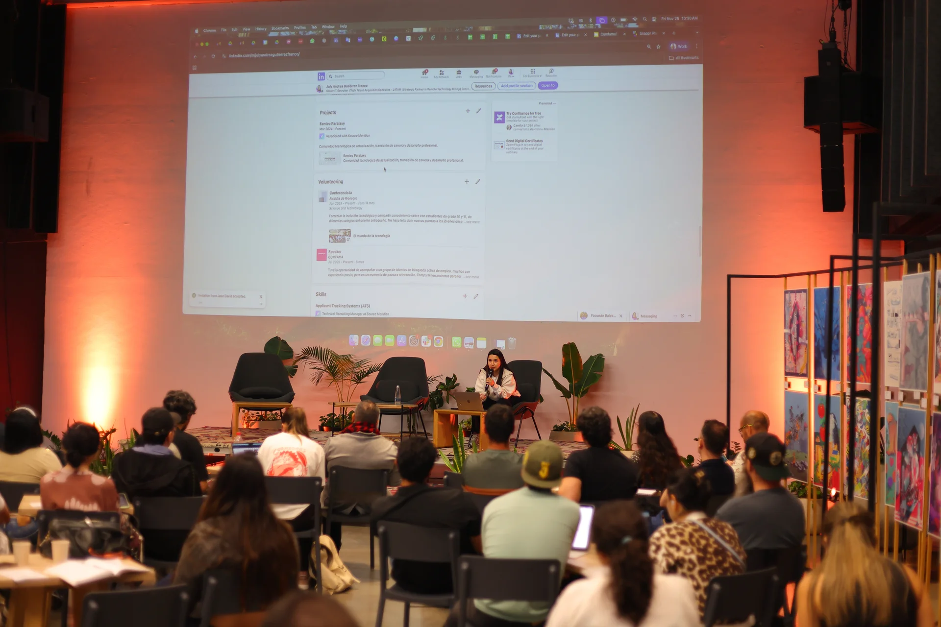 Audiencia asiste a una presentación en un auditorio, donde una persona expone frente a una pantalla con contenido proyectado